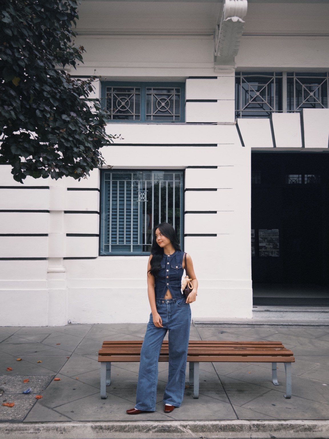 Full-length portrait of Huan Min standing beside a bench in a blue denim outfit.